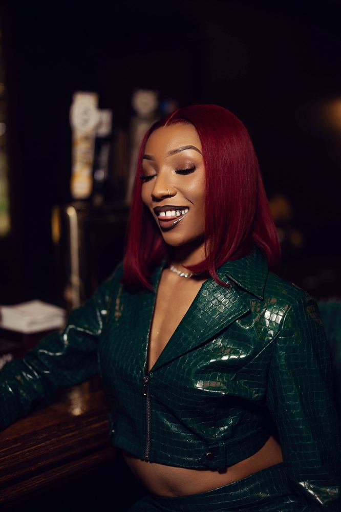 A woman with crimson hair in an emerald jacket smiling at a bar