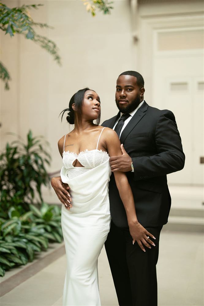 A couple in formal wear in a bright atrium with palms