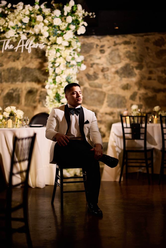 Cesar Alfaro, DC wedding and portrait photographer, seated in a white dinner jacket at a candlelit reception